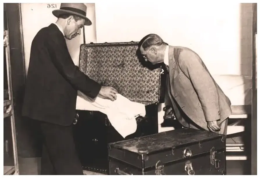 Two men are unloading a suit case from the trunk.