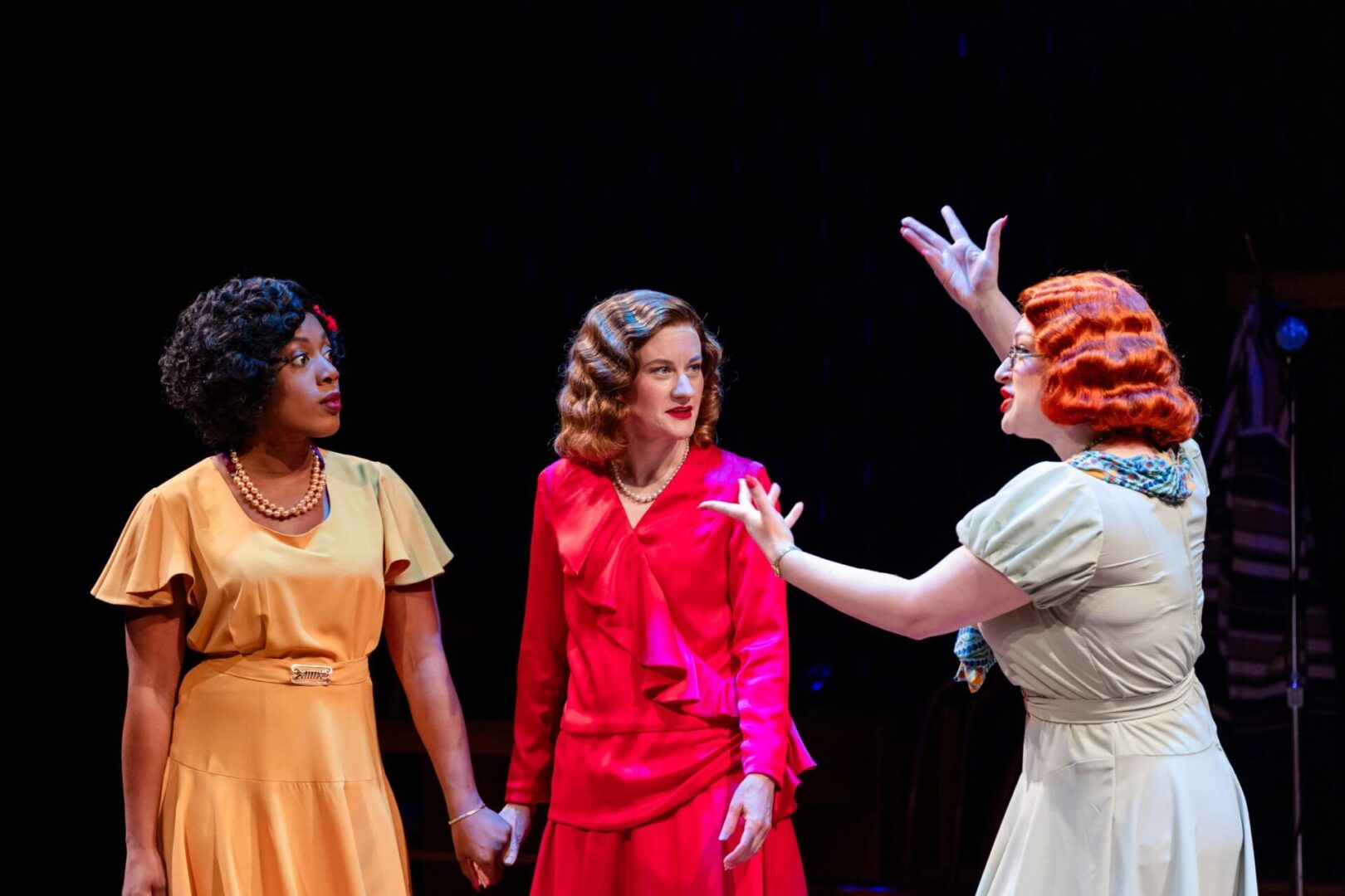 Three women in a group on stage holding hands.