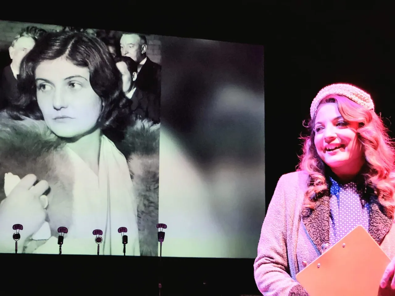 A woman standing in front of a screen with an image of a young girl.